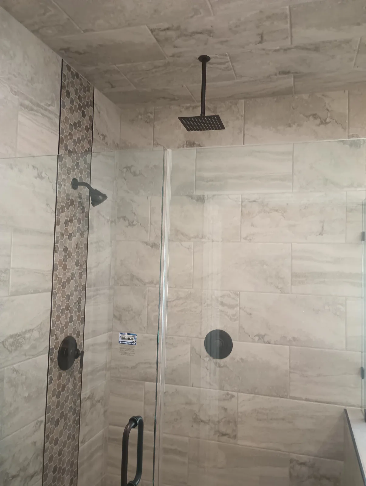Completed rainfall shower with a vertical hexagon mosaic accent strip and matte black hardware