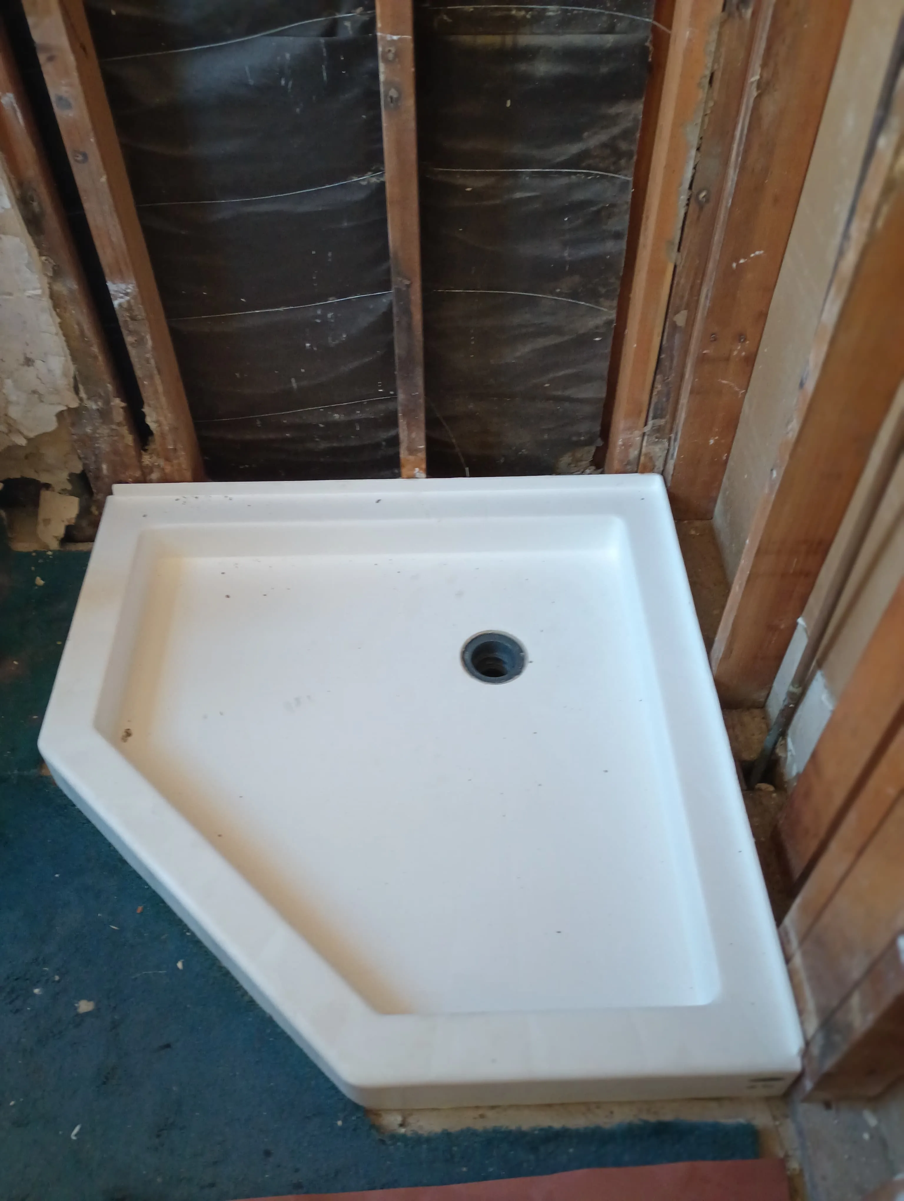 Neo-angle shower base framed against exposed wall studs